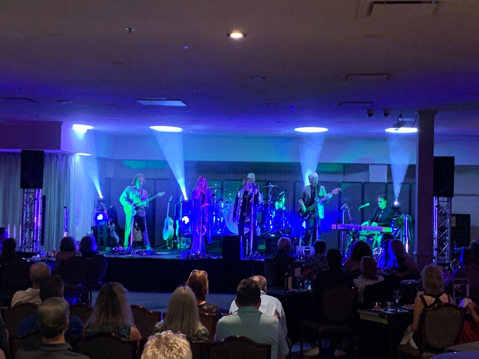 A group of people are sitting in front of a stage watching a band perform