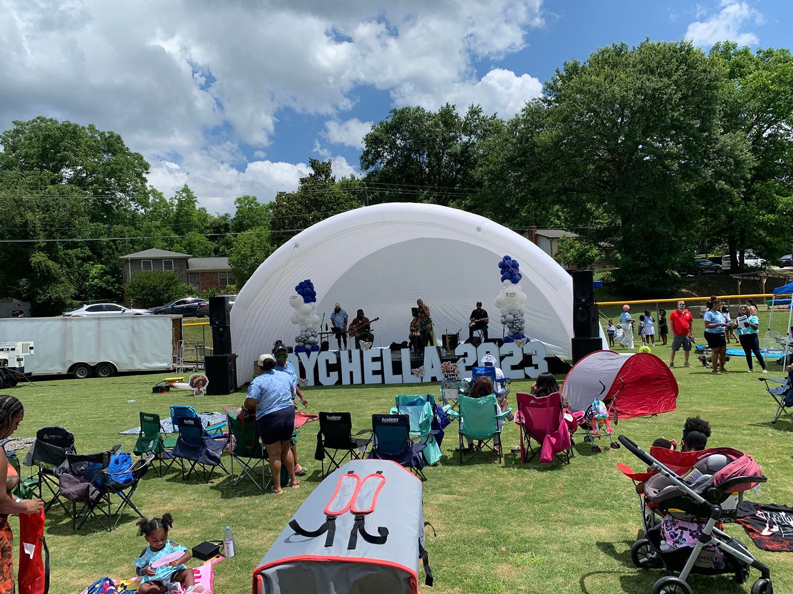 A group of people are sitting in chairs in front of an inflatable stage in a park