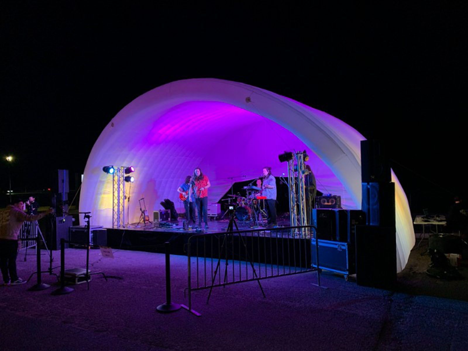 A band is playing on a stage with purple lights at night
