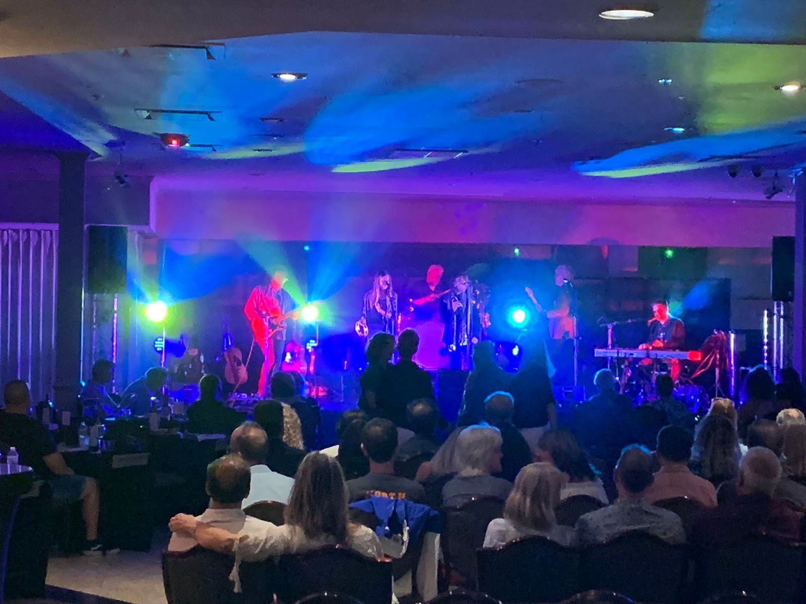 A group of people are sitting in front of a stage watching a band perform