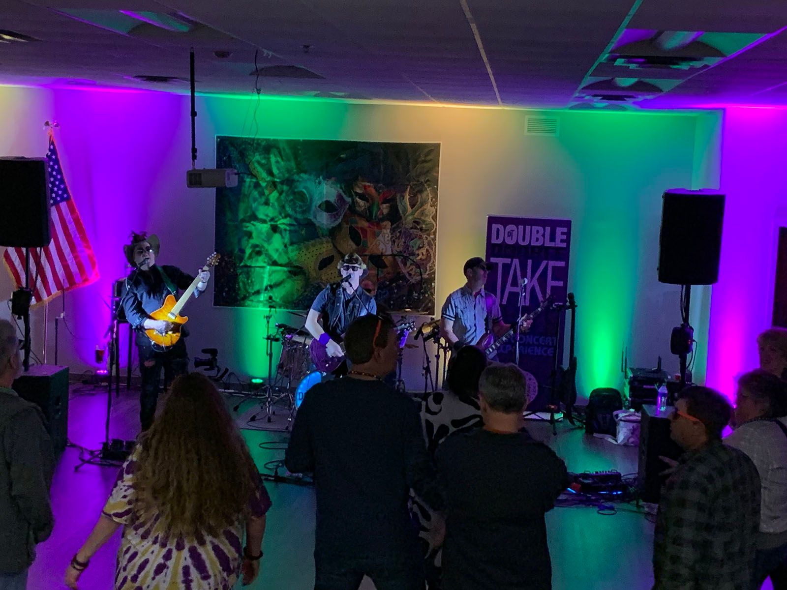 A group of people are standing in a room watching a band perform on stage