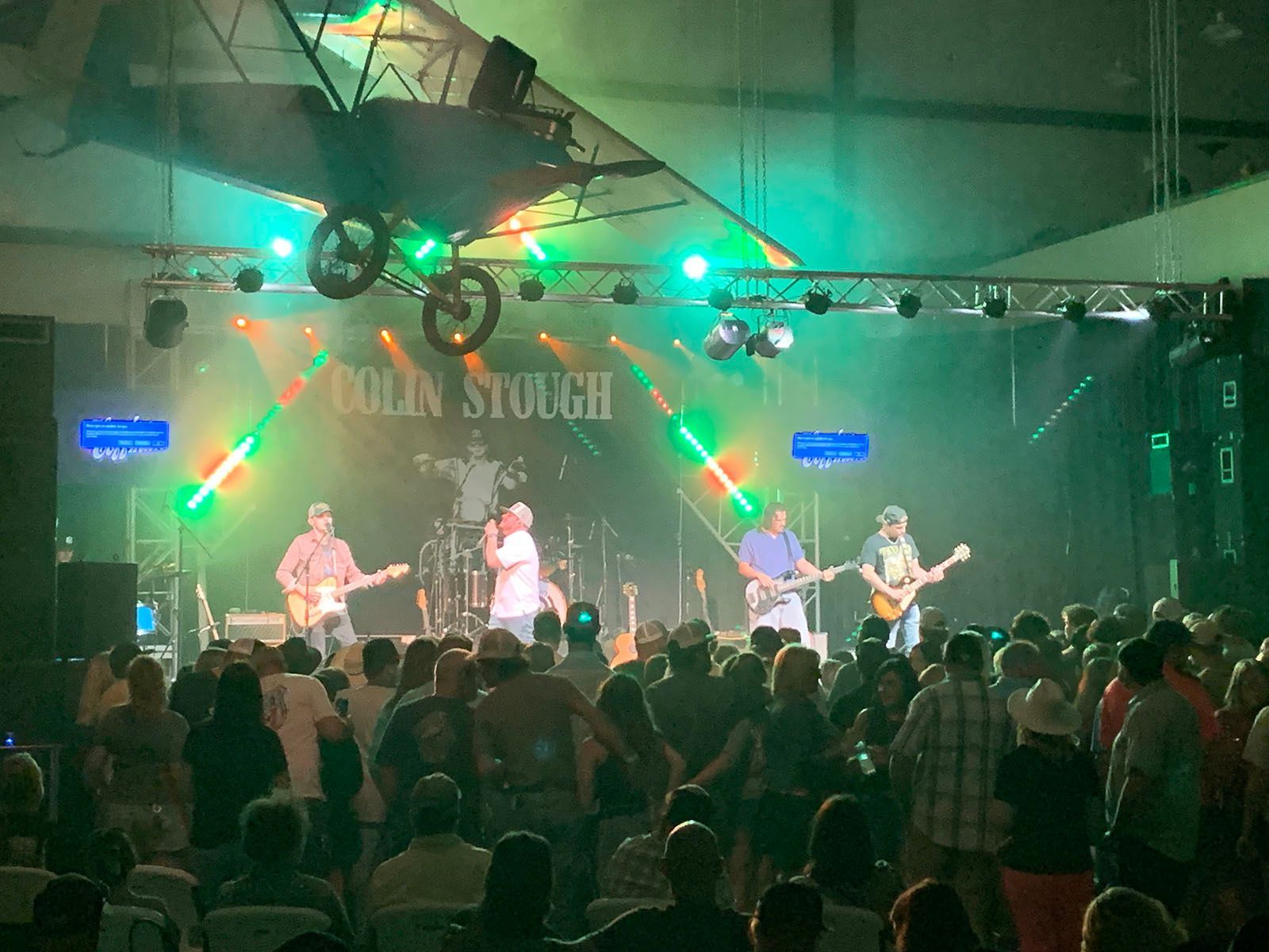 A group of people are standing in front of a stage with a plane hanging from the ceiling