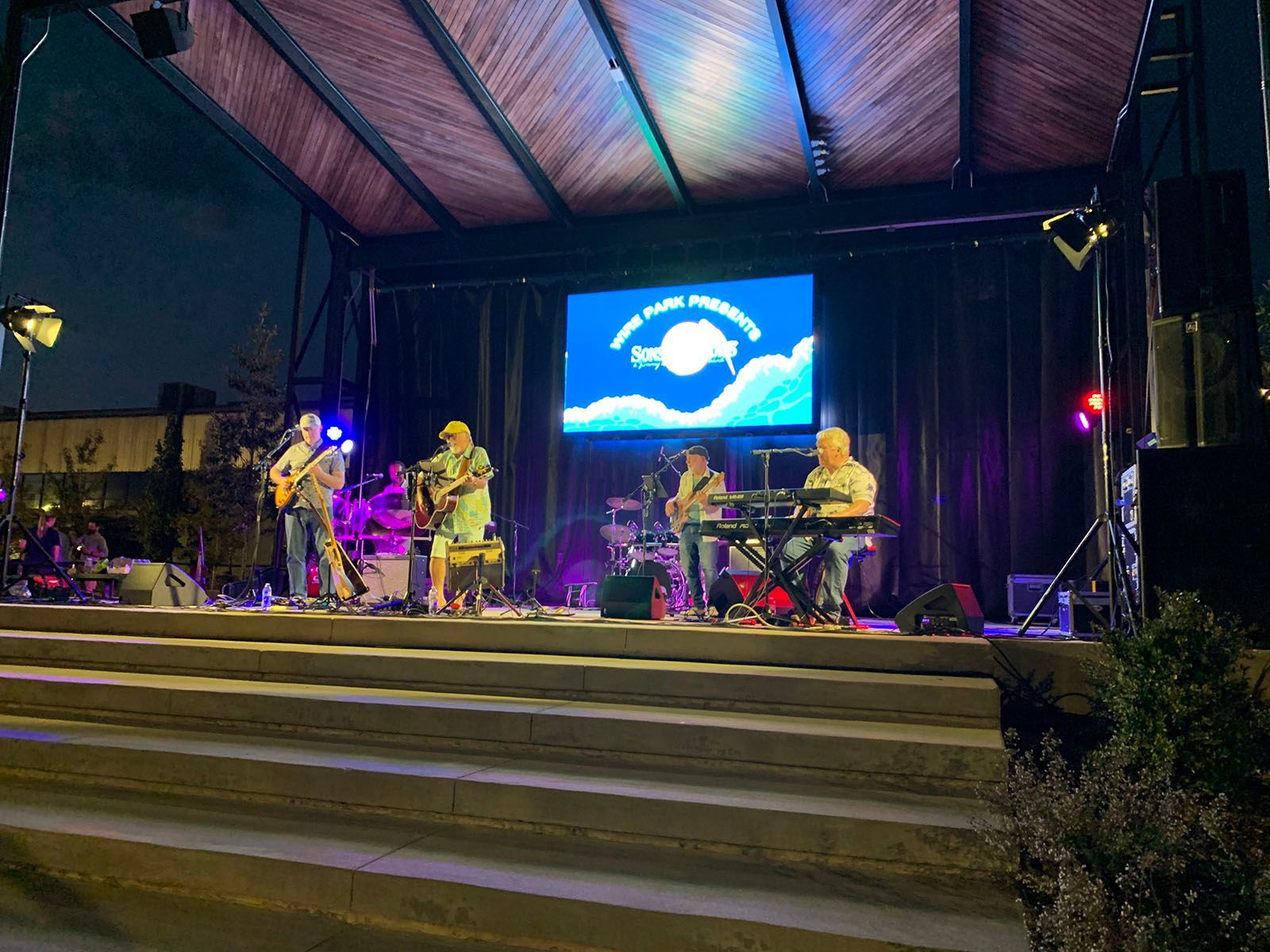 A band playing instruments on a stage in front of a large screen