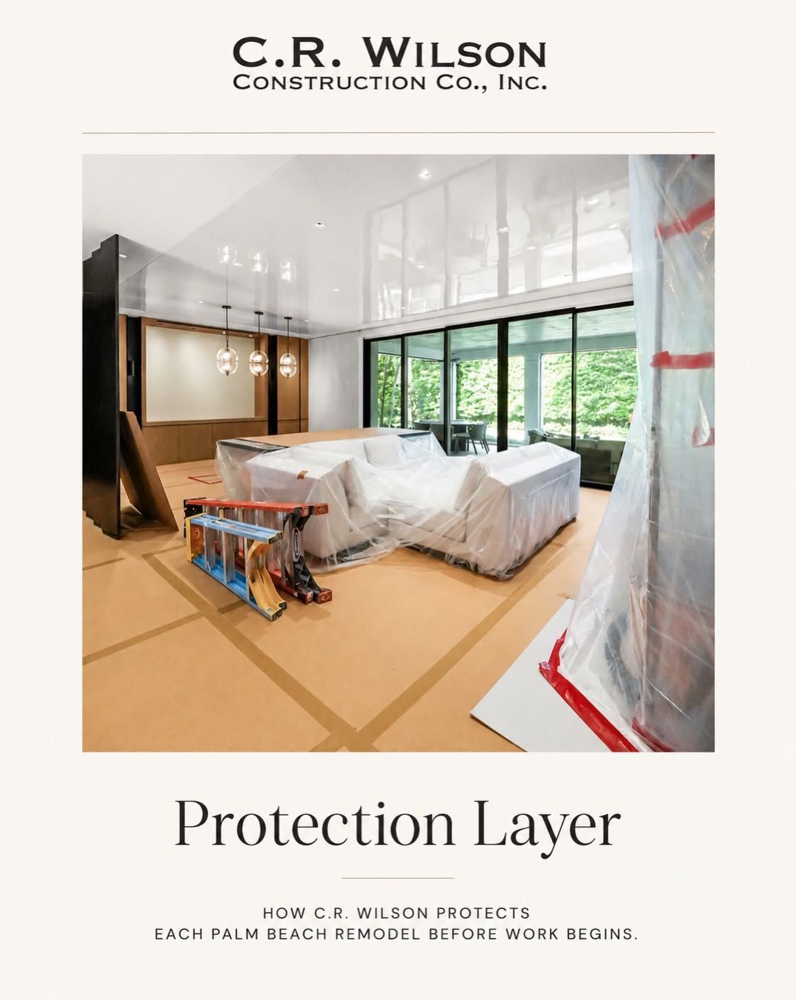Construction site with furniture covered in protective plastic and a floor tarp under a large window.