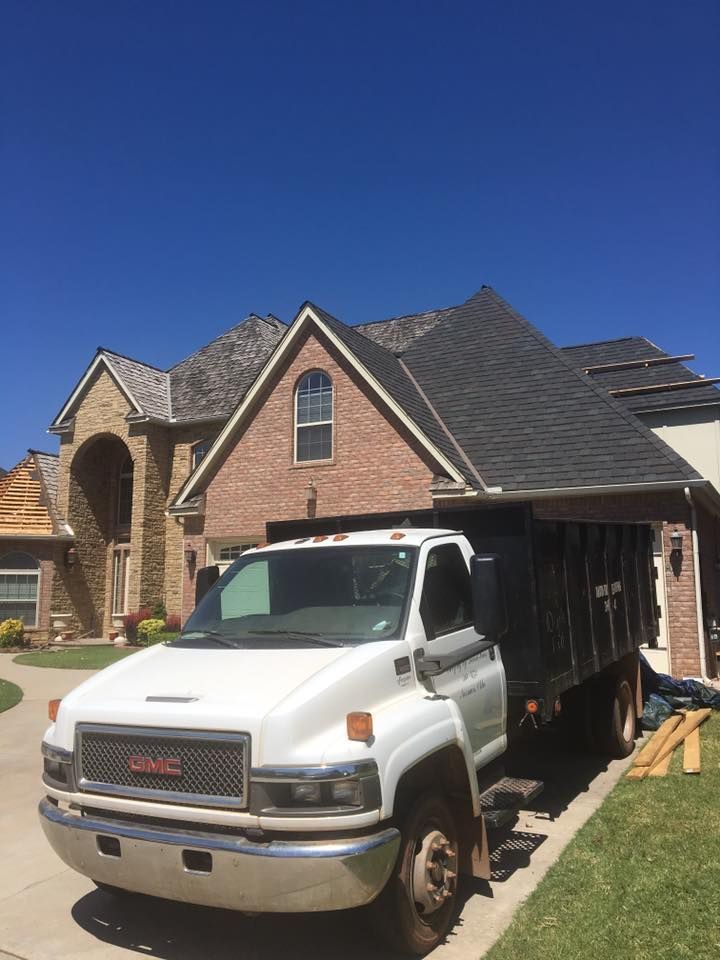 White GMC truck parked in front of a house, possibly for roofing work. Bright blue sky.