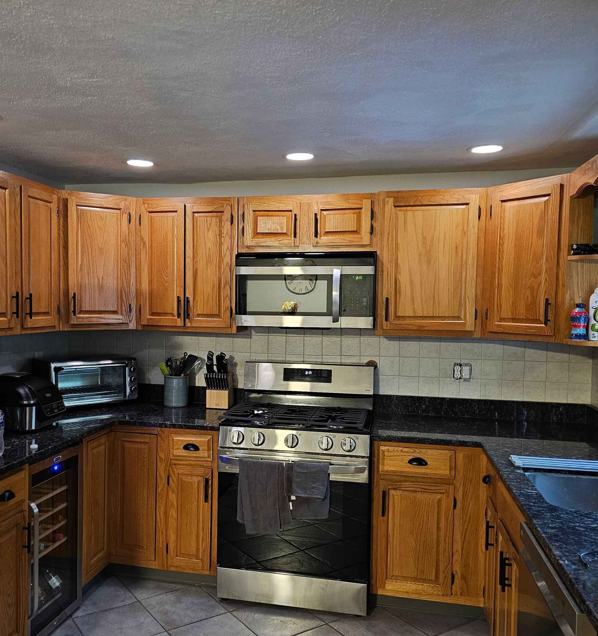 Wooden kitchen cabinets surround a stainless steel oven and microwave. Black countertops and tile backsplash.
