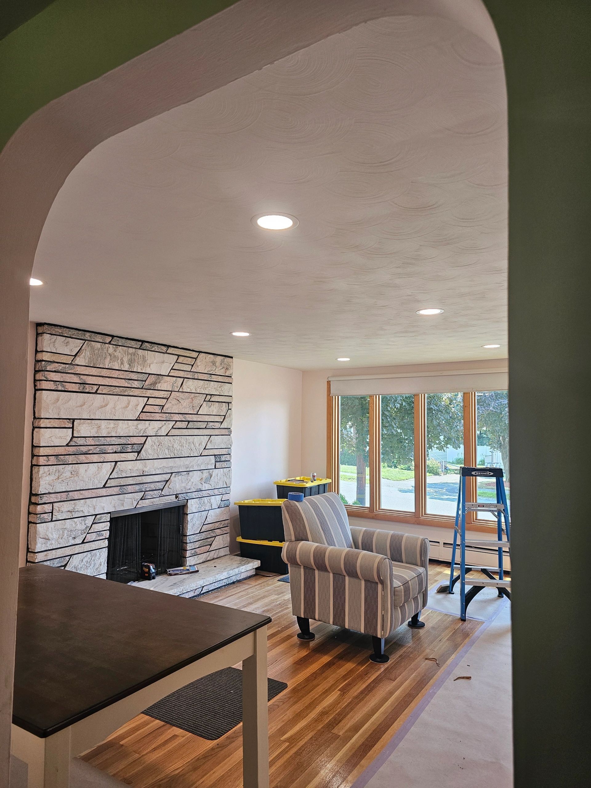 Living room renovation with stone fireplace, wood floors, arched doorway, and two armchairs.