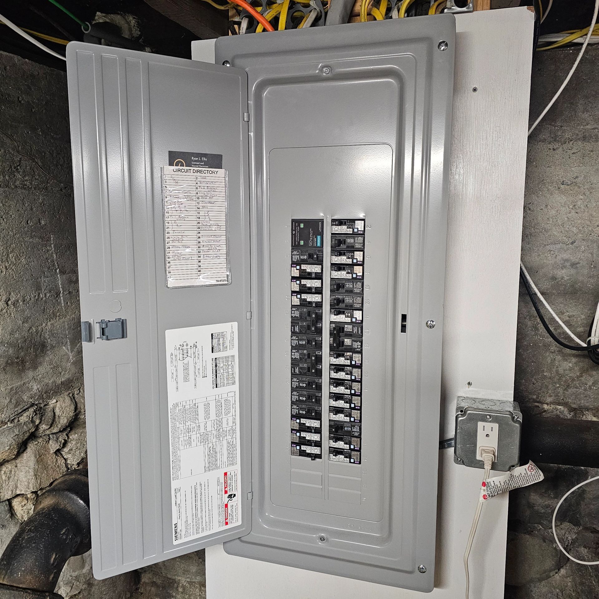 Electrical circuit breaker panel with open door, mounted on a white wall in a basement.