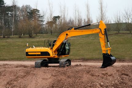 A yellow excavator parked on a dirt mound in an outdoor field with trees in the background.