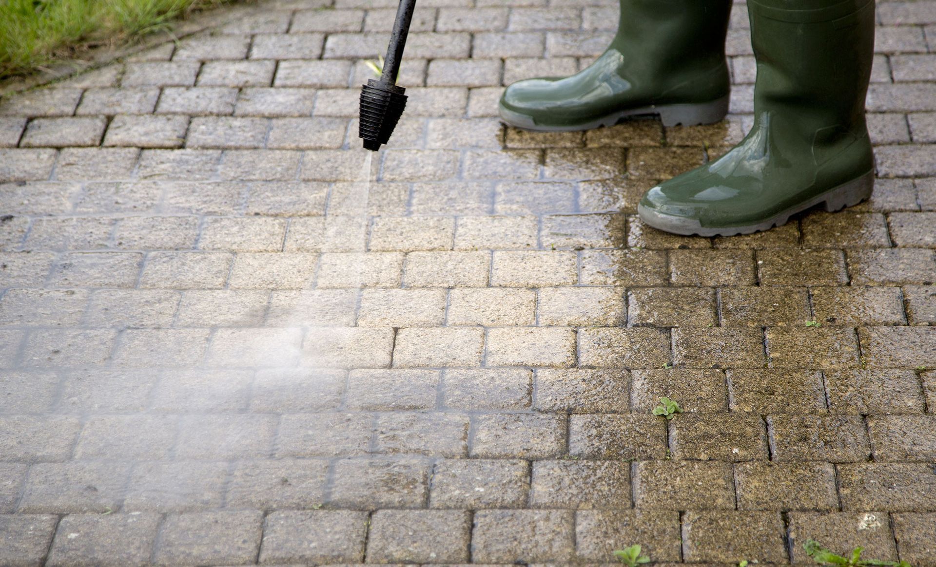 A person is cleaning a brick walkway with a high pressure washer.