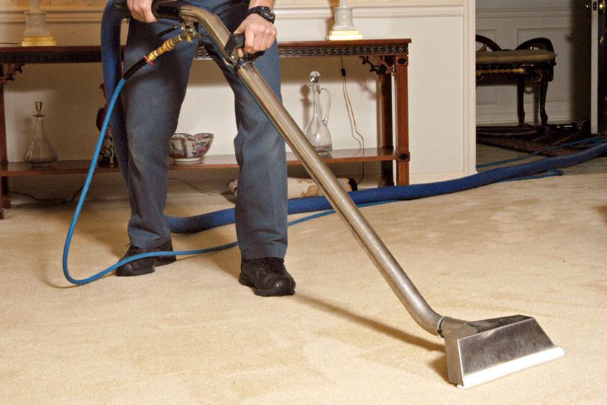 A man is cleaning a white carpet with a vacuum cleaner.