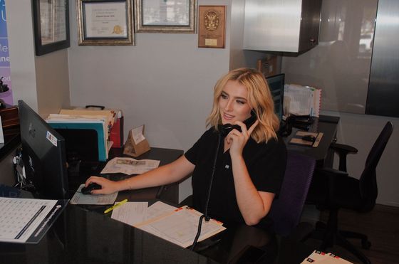 Learn More About Family Dentistry Woman at desk talking on phone, using computer, paperwork visible.