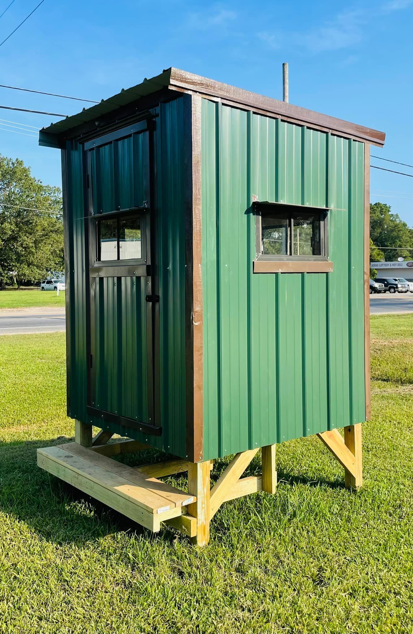 A green shed is sitting in the middle of a grassy field.