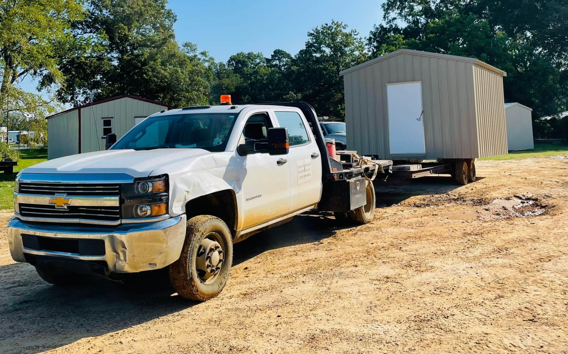 A white truck is towing a small shed on a trailer.