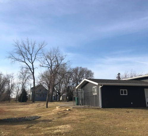 A dark gray building with a chain link fence, and bare trees under a blue sky.
