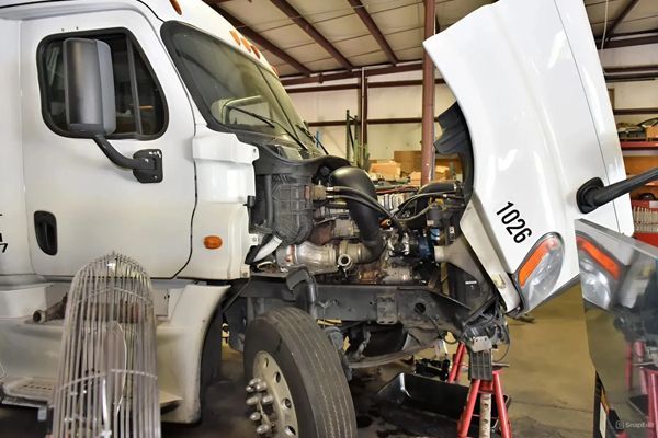 A white truck with the hood up is being worked on in a garage.