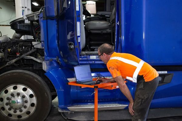 A man in an orange shirt is working on a blue semi truck.