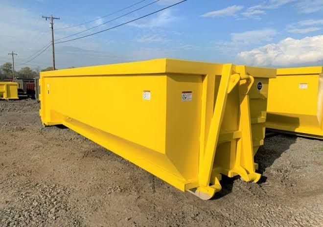 Yellow metal roll-off dumpster on a dirt surface, with structural supports on the sides.
