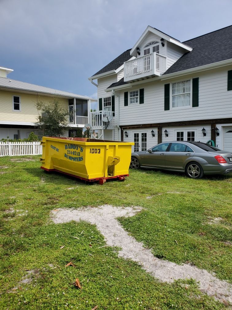 A yellow dumpster is parked in front of a house. Roll-Off Dumpster Rental in Sarasota.