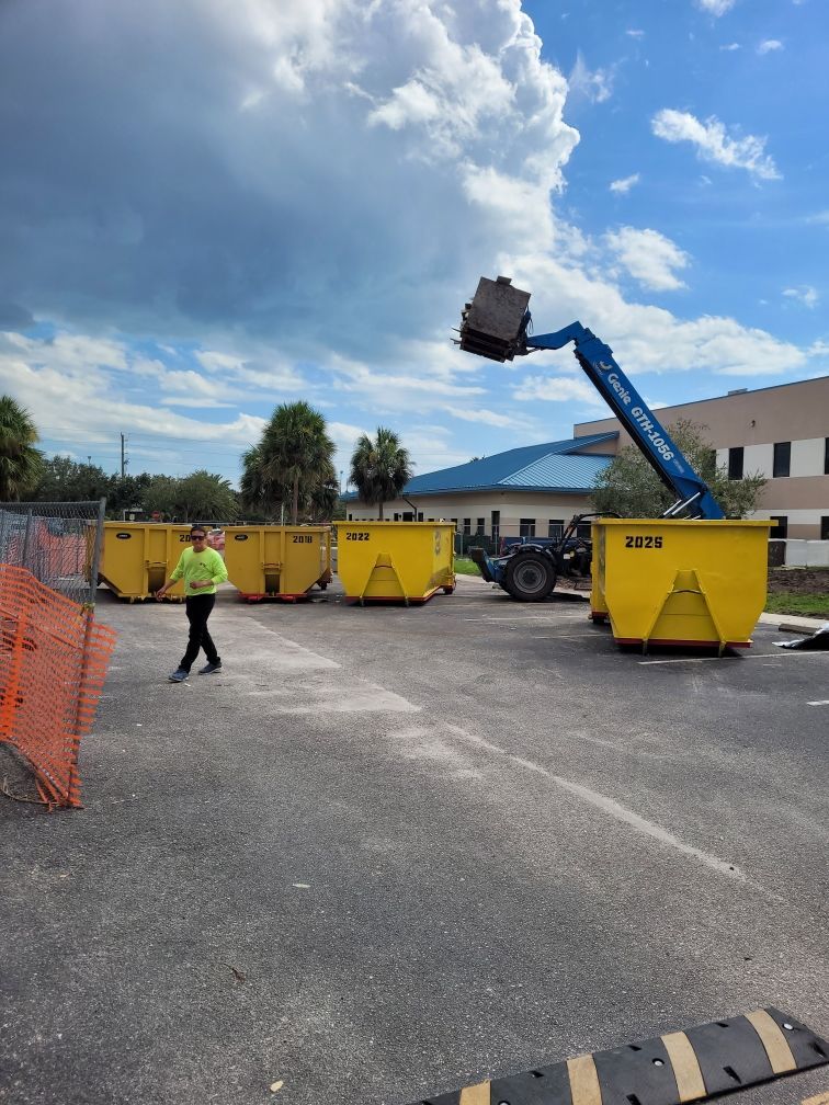 A man is standing in a parking lot next to a row of yellow dumpsters. Roll-Off Dumpster Rental in Sarasota.