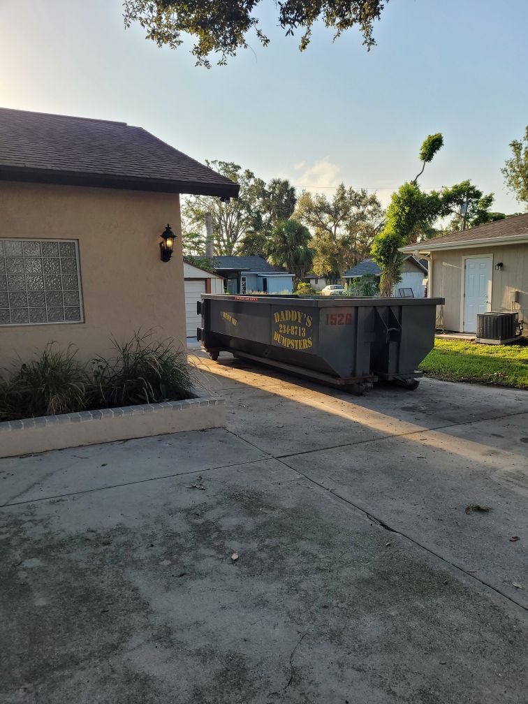 A dumpster is parked in front of a house in a driveway. Roll-Off Dumpster Rental in Sarasota.