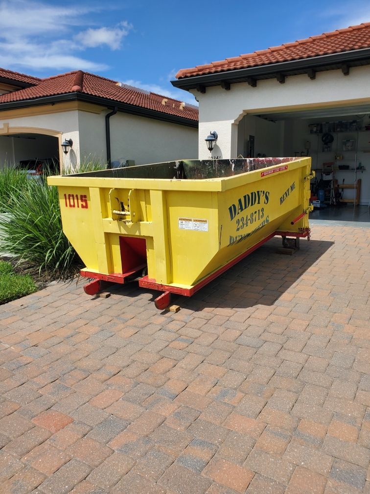 A yellow dumpster is parked in front of a house on a brick driveway. Roll-Off Dumpster Rental in Sarasota.
