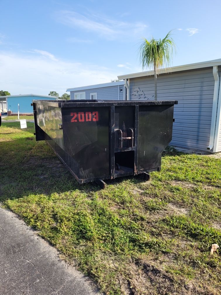 A dumpster is sitting in the grass next to a road. Roll-Off Dumpster Rental in Sarasota.