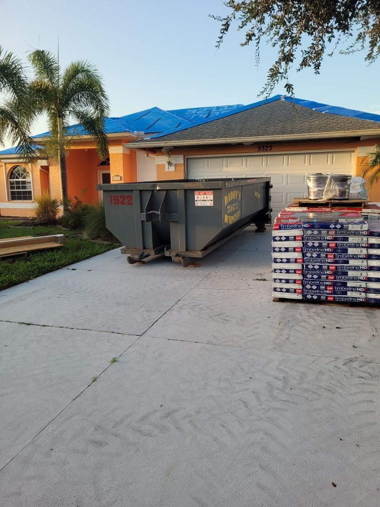 A dumpster is in front of a house with a blue tarp on the roof. Roll-Off Dumpster Rental in Sarasota.