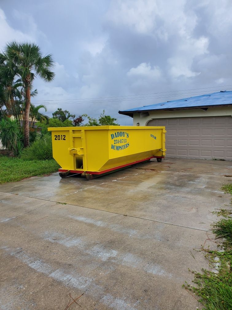 A yellow dumpster is parked in a driveway next to a garage. Roll-Off Dumpster Rental in Sarasota.