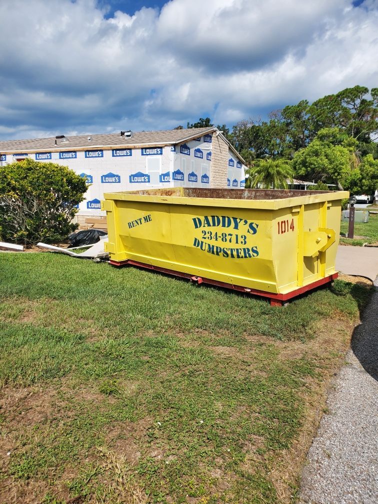 A yellow dumpster is sitting in the grass in front of a building. Roll-Off Dumpster Rental in Sarasota.