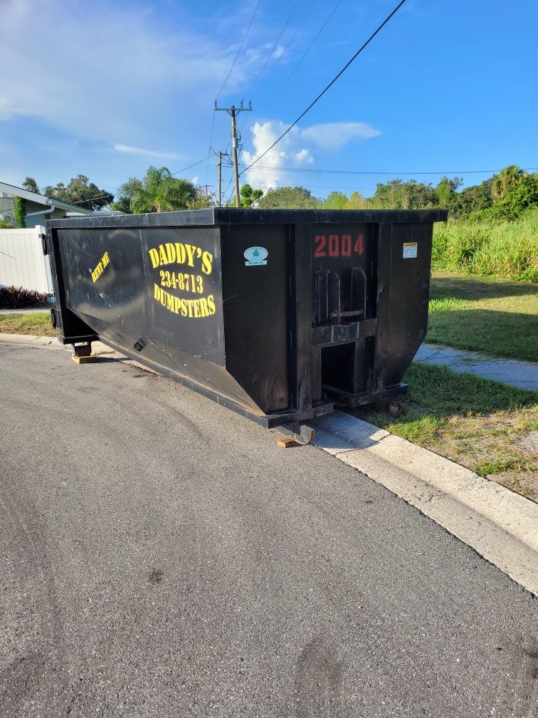 A black dumpster is parked on the side of the road. Roll-Off Dumpster Rental in Sarasota.