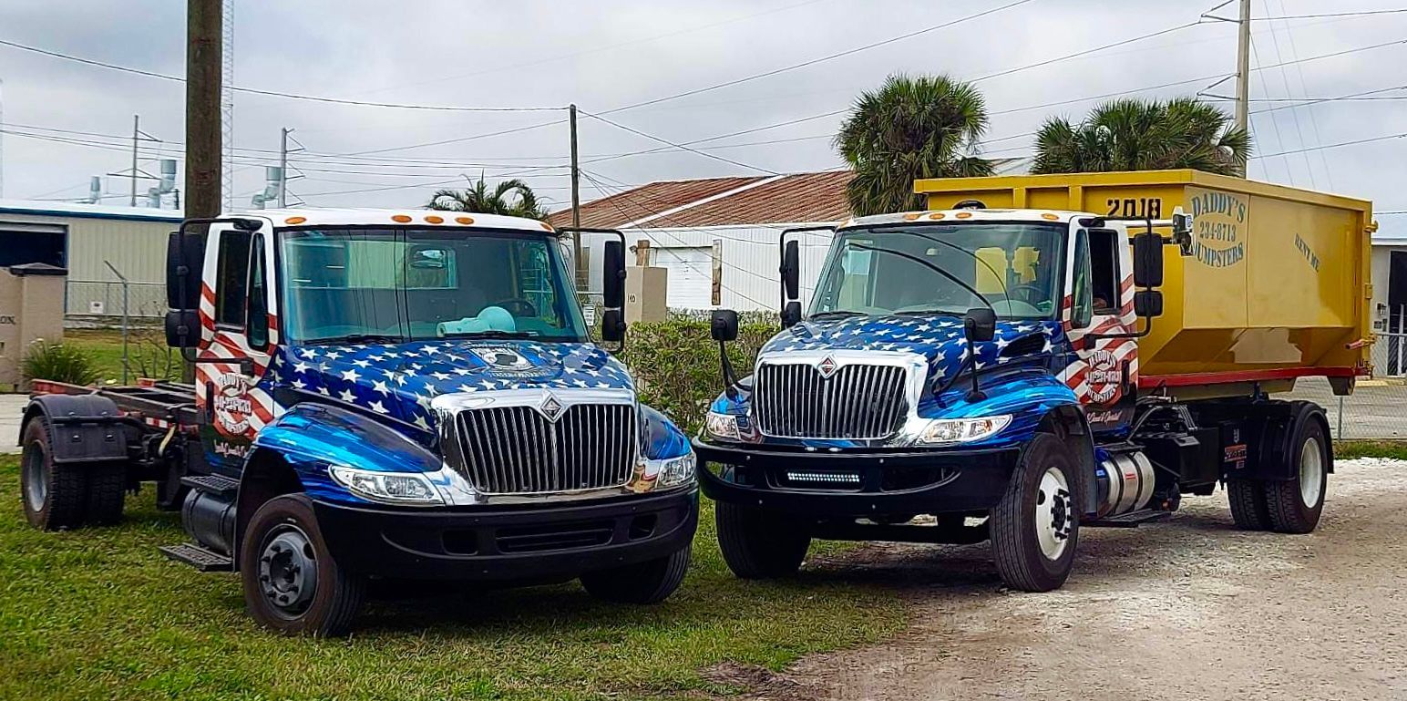 Two dump trucks are parked next to each other in a grassy area. Roll-Off Dumpster Rental in Sarasota.