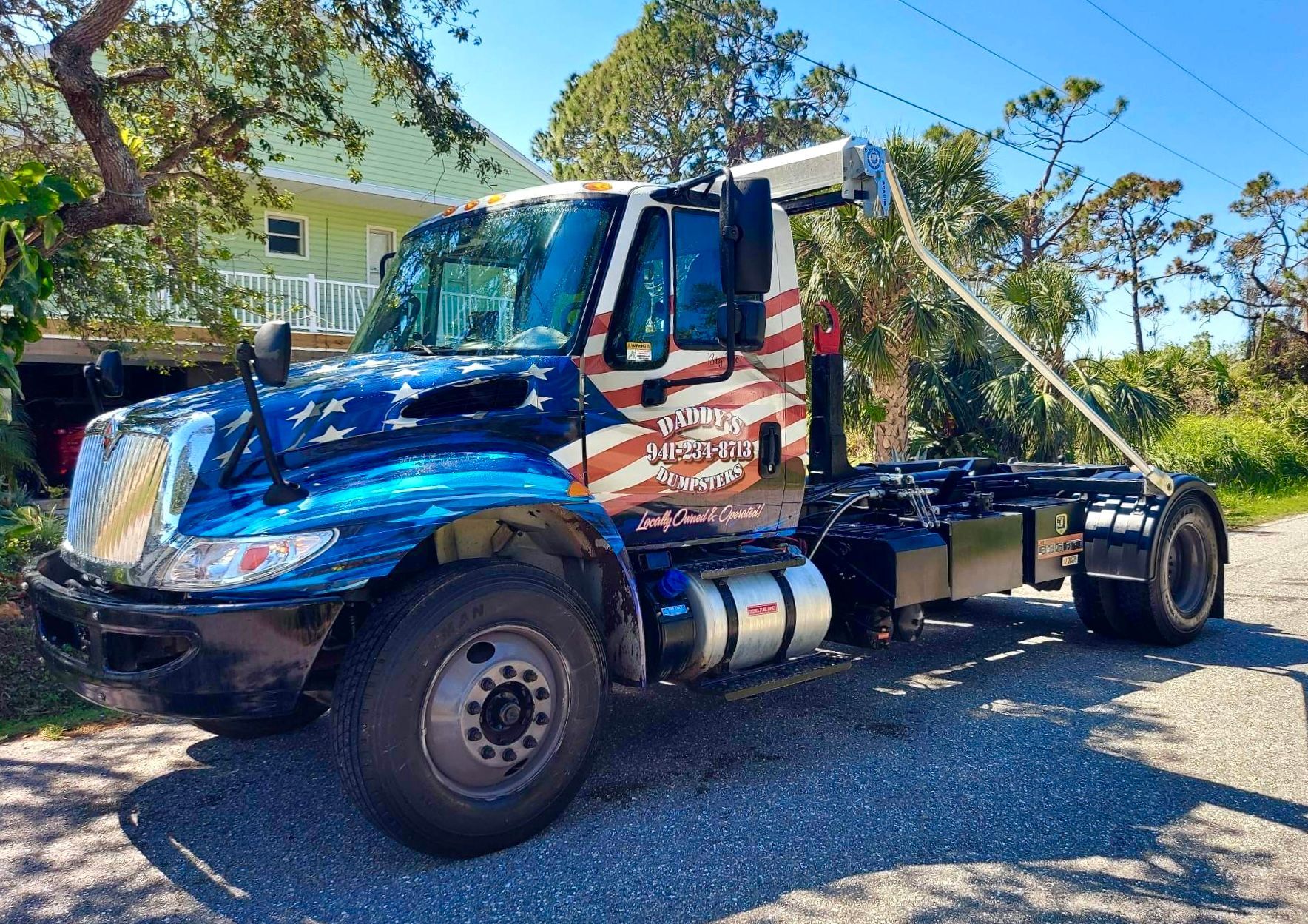 A blue and red dump truck is parked in front of a house. Roll-Off Dumpster Rental in Sarasota.