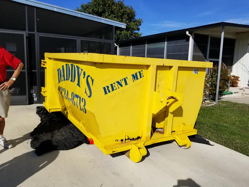 A man standing next to a yellow dumpster that says Rent me. Roll-Off Dumpster Rental in Sarasota.