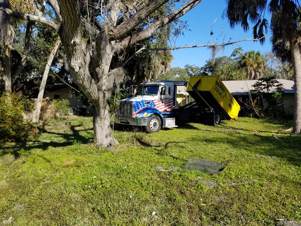 A dump truck is parked in a grassy yard next to a tree. Roll-Off Dumpster Rental in Sarasota.