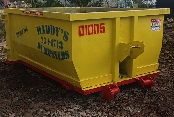 A neat-looking yellow dumpster for Daddy's Dumpsters is sitting on the ground. Roll-Off Dumpster Rental in Sarasota.