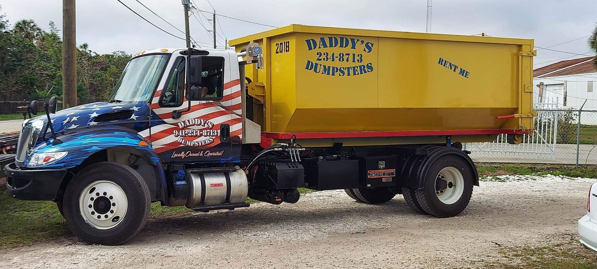A dump truck with an American flag painted on it is parked in a gravel lot. Roll-Off Dumpster Rental in Sarasota.