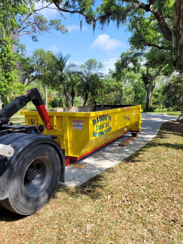 A yellow dumpster is sitting on the side of a road next to a truck. Roll-Off Dumpster Rental in Sarasota.