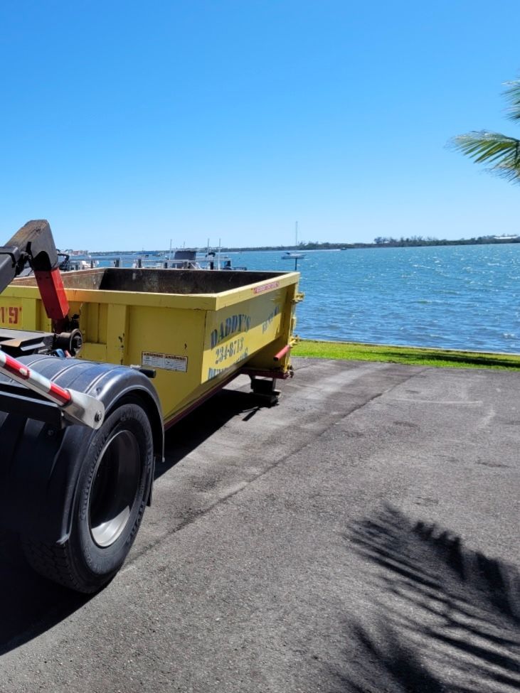 A yellow dumpster is parked next to a body of water. Roll-Off Dumpster Rental in Sarasota.