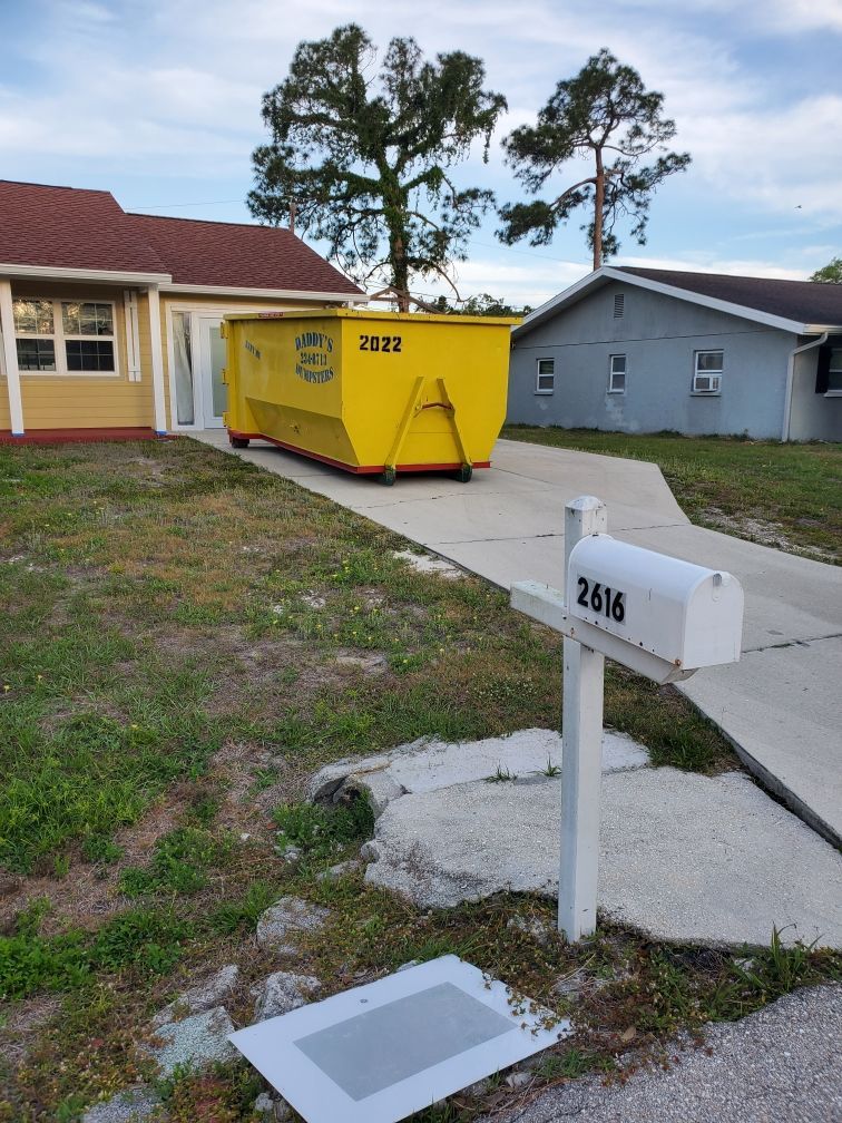A yellow dumpster is parked in front of a house next to a mailbox. Roll-Off Dumpster Rental in Sarasota.