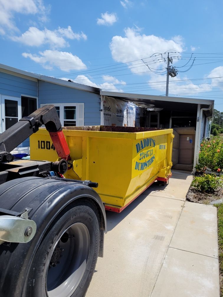 A yellow dumpster is sitting on the side of a truck in front of a house. Roll-Off Dumpster Rental in Sarasota.