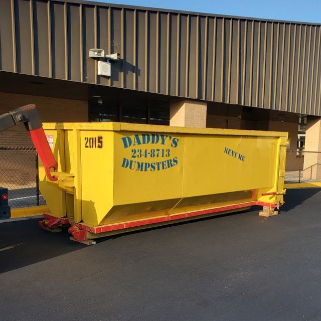 Yellow dumpster with 'Daddy's Dumpsters' logo, parked outside a building.