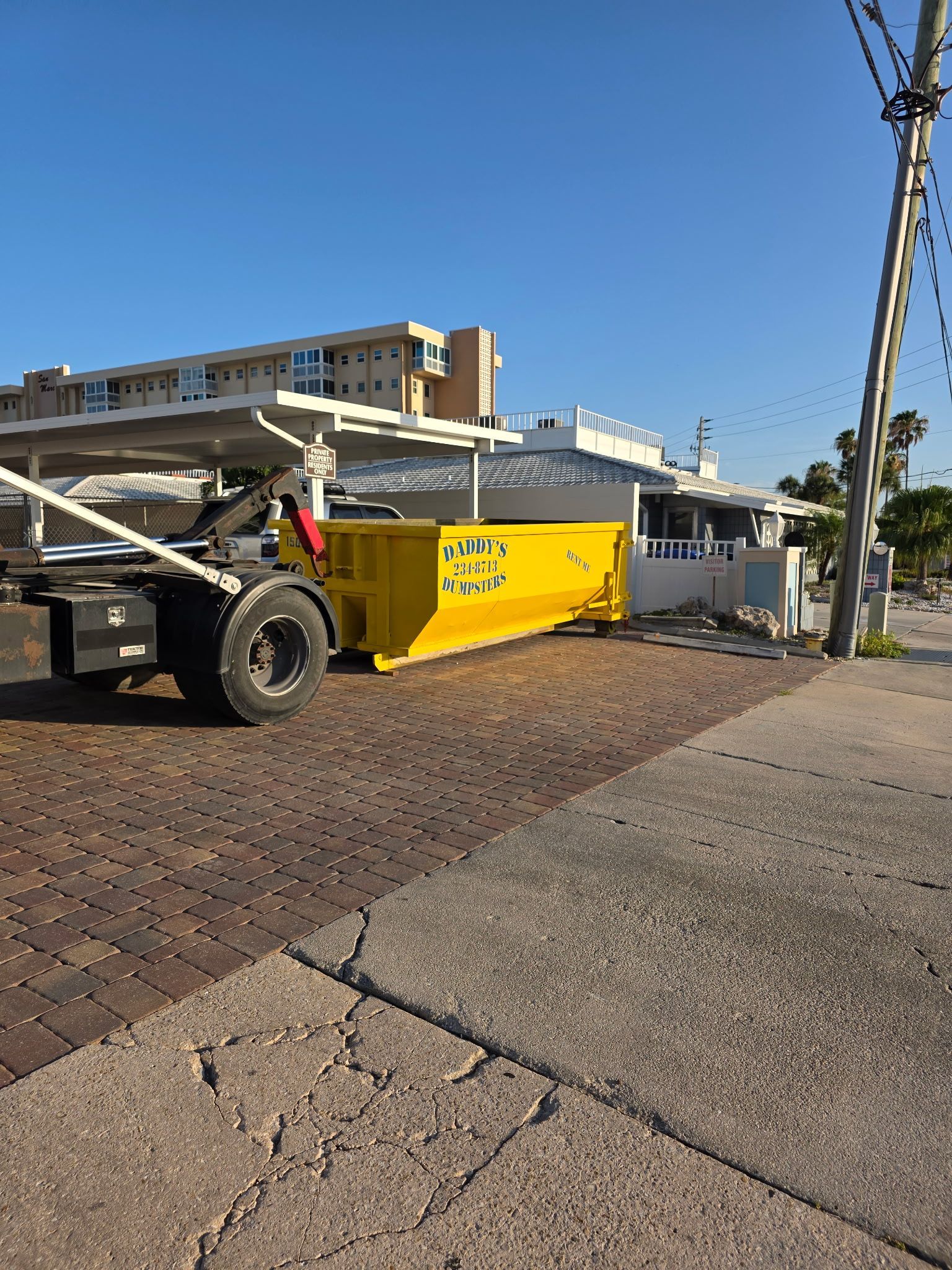 15-yard yellow dumpster truck parked on a brick driveway beside houses under a blue sky.
