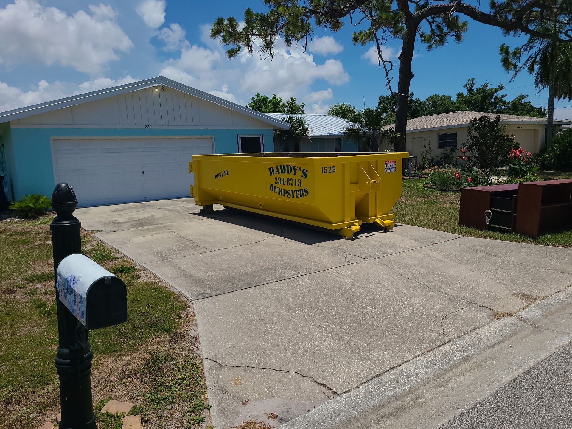 15-yard yellow dumpster in a driveway in front of a white garage and suburban house.