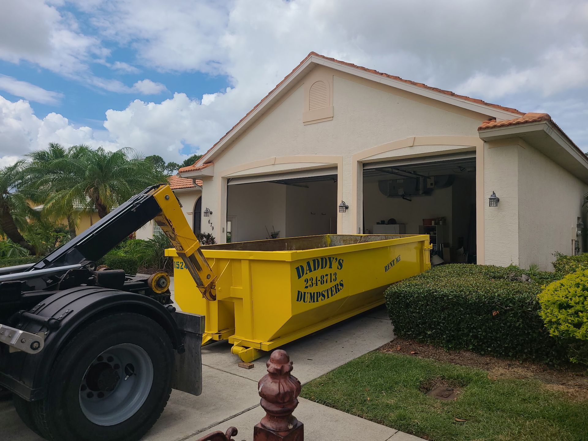 15-yard yellow dumpster being loaded onto a truck in front of a suburban house and garage