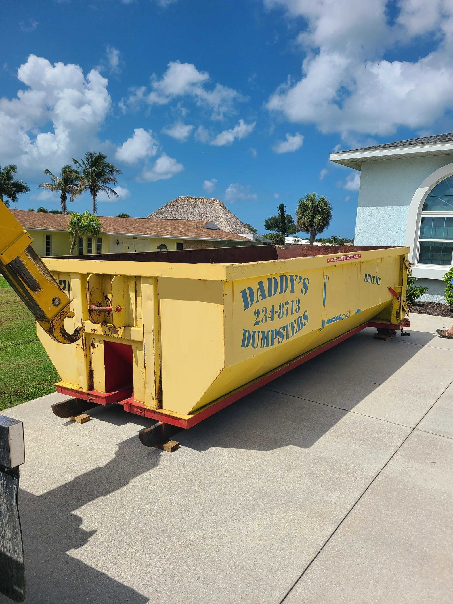 15-yard yellow construction dumpster on a concrete driveway beside a house under a bright blue sky