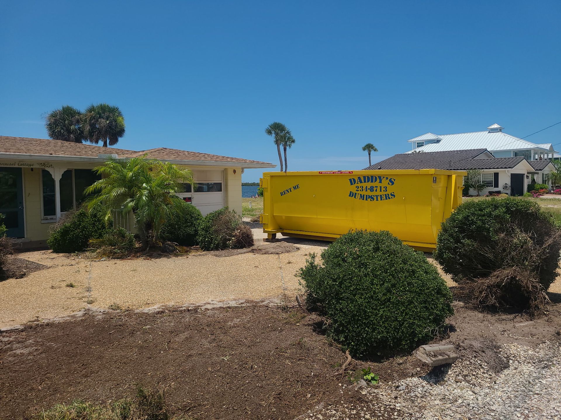 20-yard yellow dumpster in a desert-style yard beside a low house under a clear blue sky.