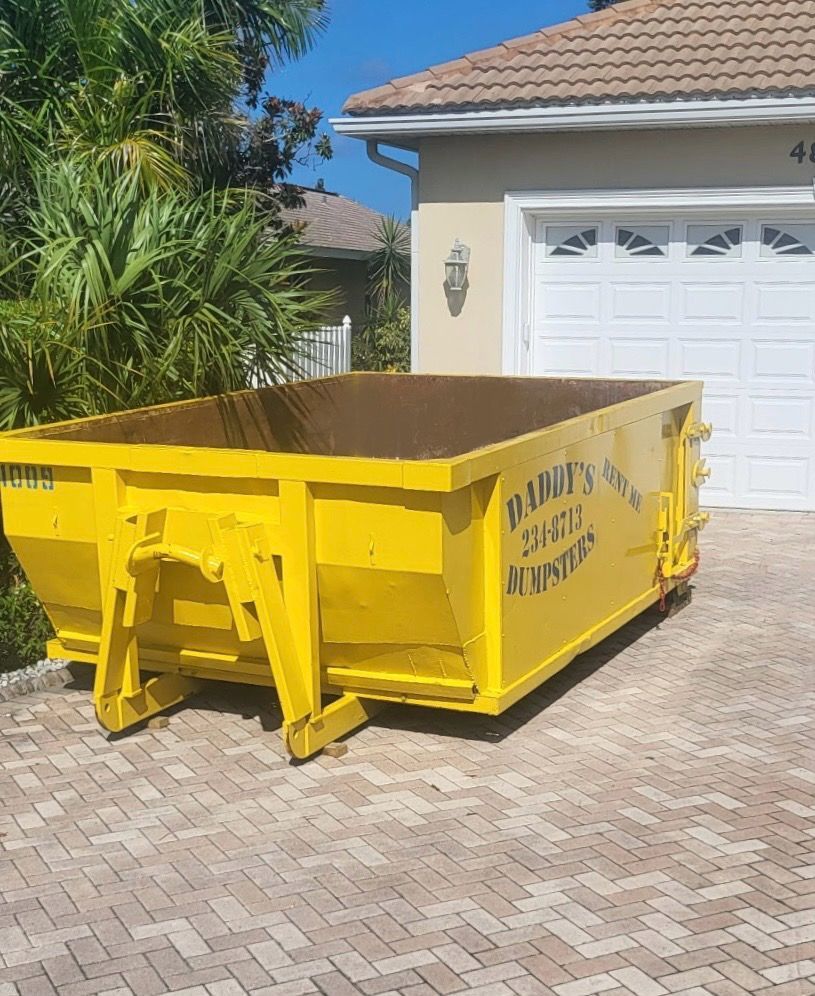 10-yard yellow dumpster on a driveway in front of a white garage door, beside a house and palm trees.