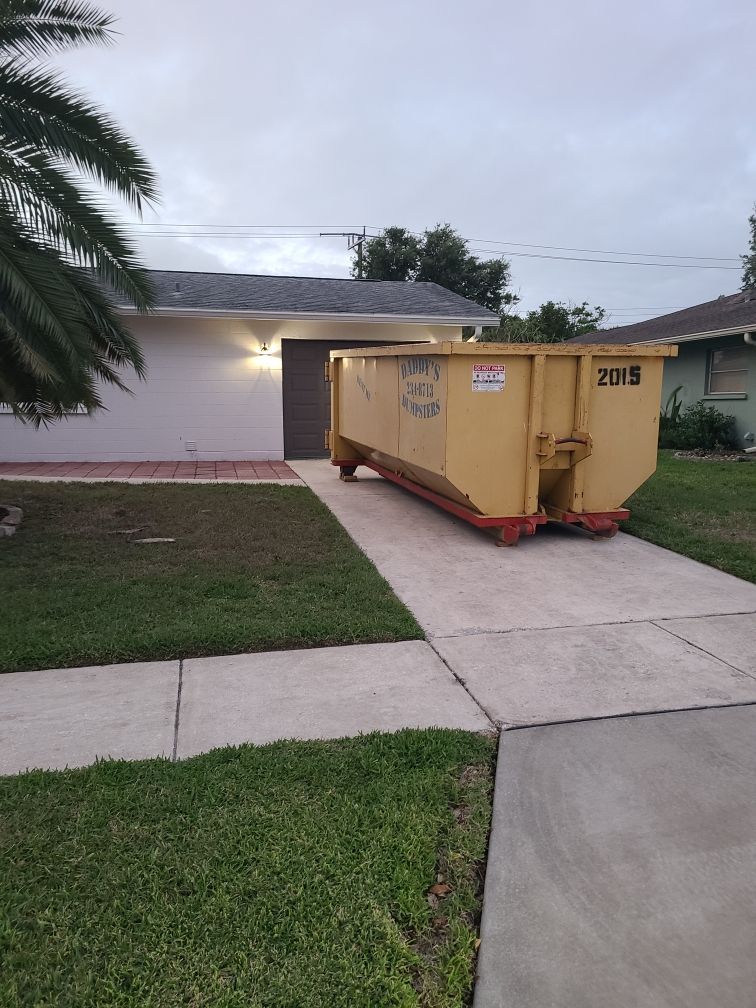 20-yard yellow dumpster in a driveway beside a white house and green lawn at dusk