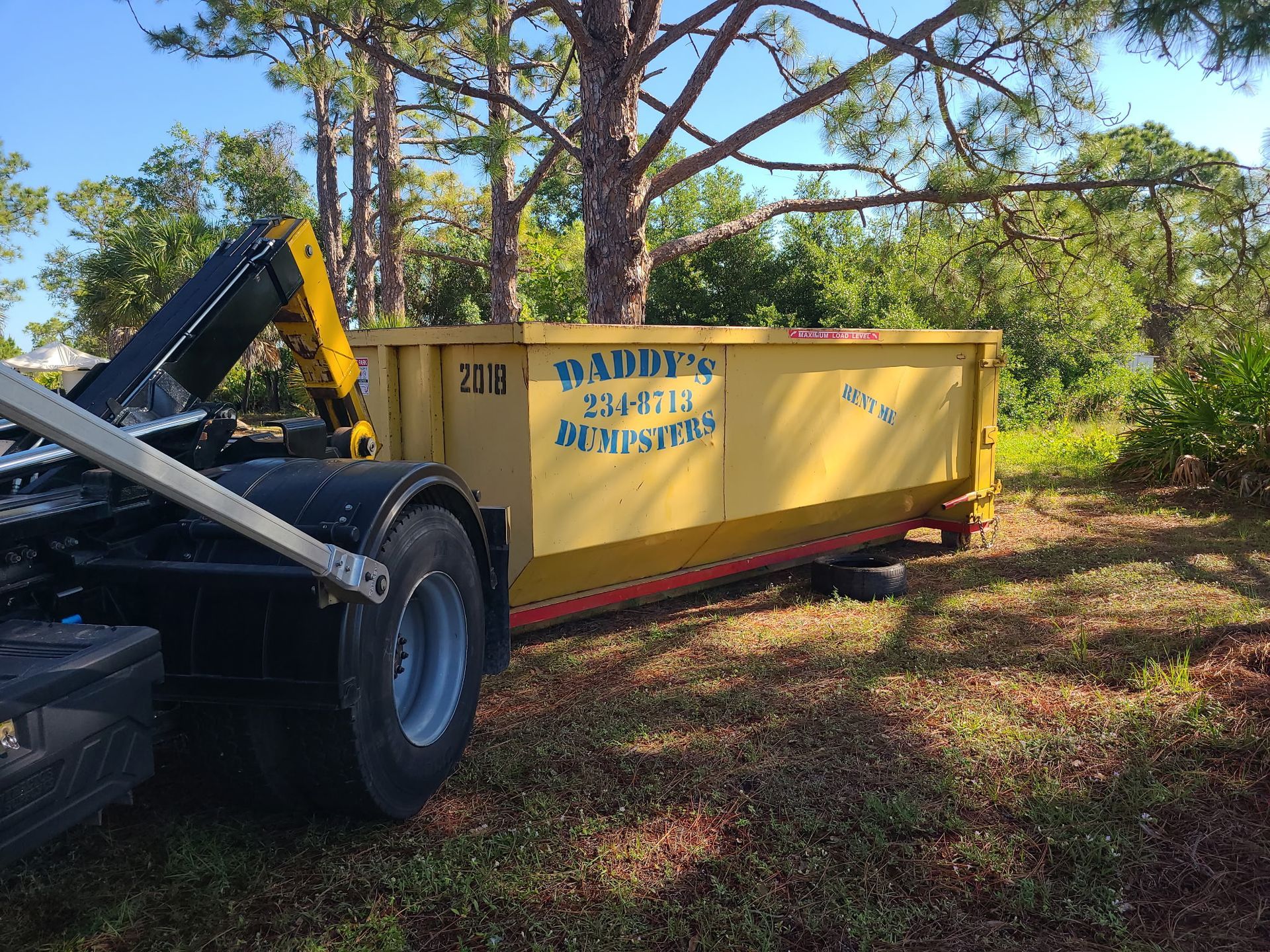 20-yard yellow dumpster in a wooded area being loaded by a front-end loader.